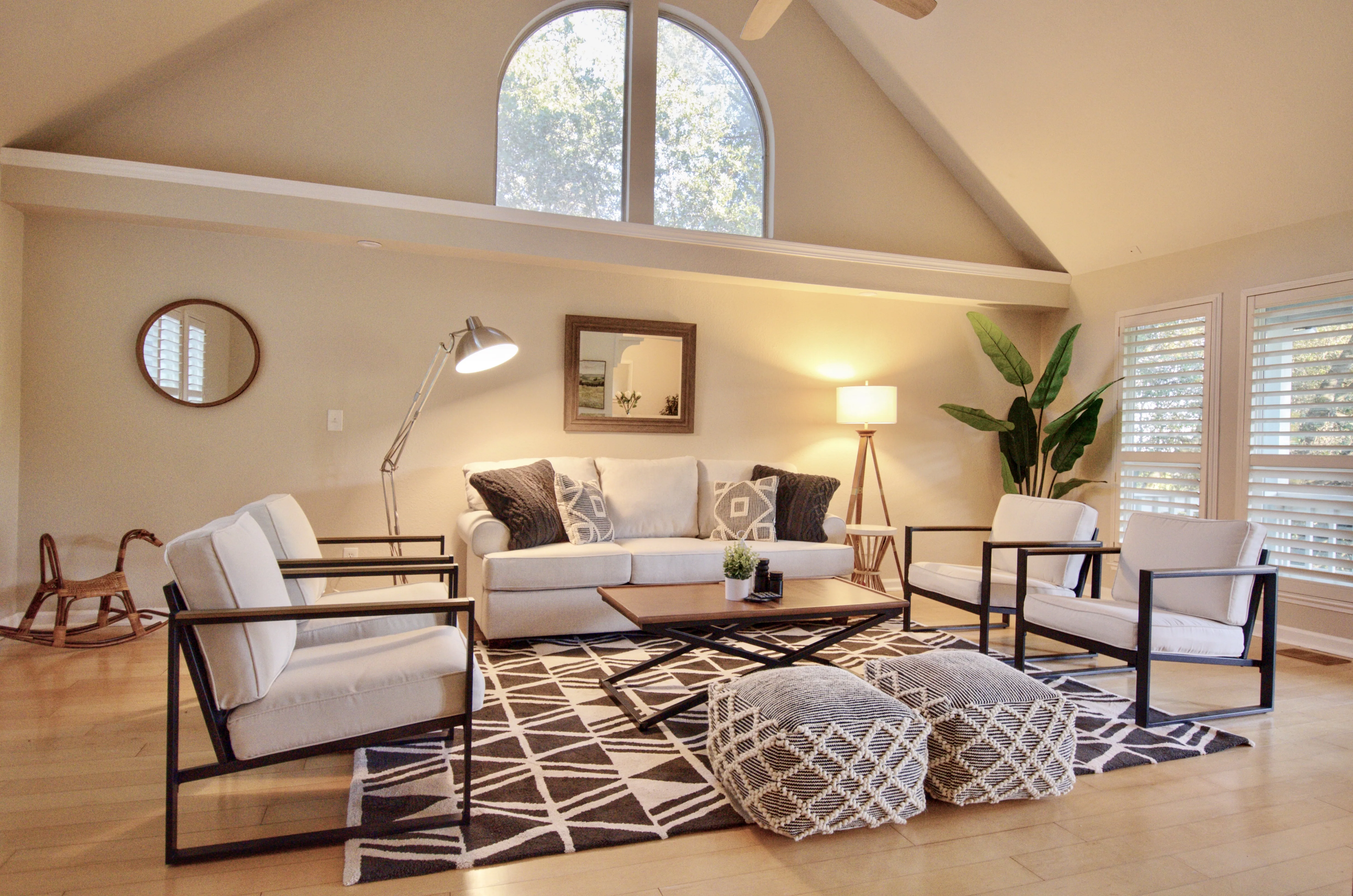 Bright modern living room with white sofa, mid-century armchairs, wooden coffee table, geometric area rug, arched window, and decorative lighting